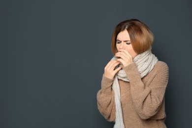 Woman suffering from cough on dark background. Space for text