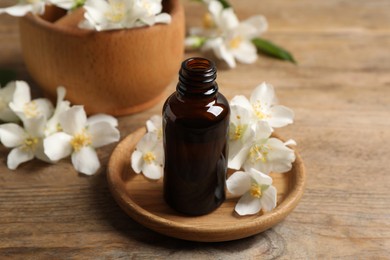 Photo of Jasmine essential oil and fresh flowers on wooden table