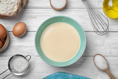 Batter for thin pancakes and products on white wooden table, flat lay