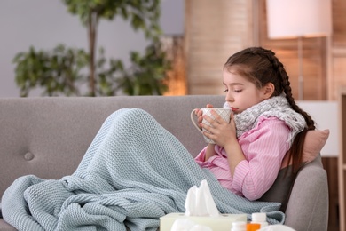 Photo of Little girl with cup of hot drink suffering from cold on sofa at home