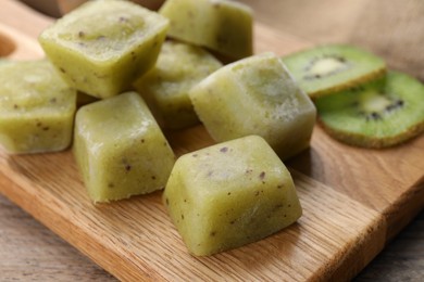 Frozen kiwi puree cubes and ingredient on wooden table, closeup