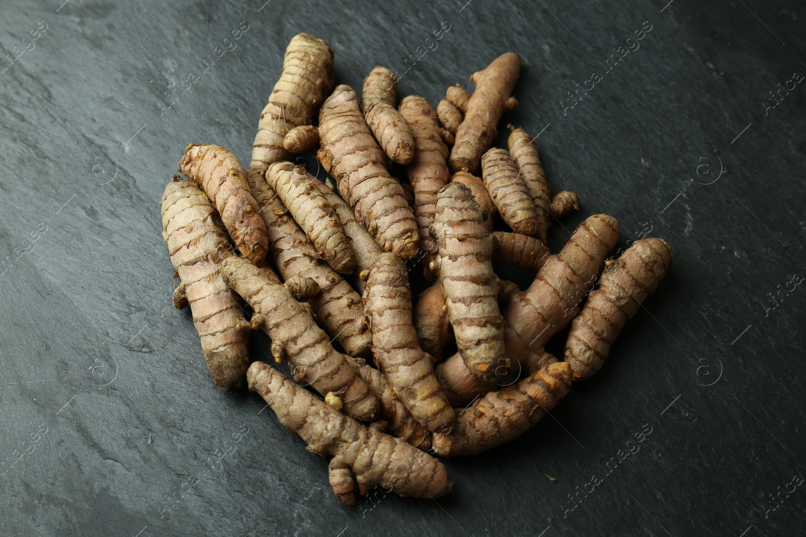 Photo of Many raw turmeric roots on black textured table, above view