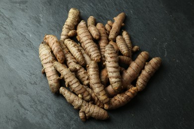 Many raw turmeric roots on black textured table, above view
