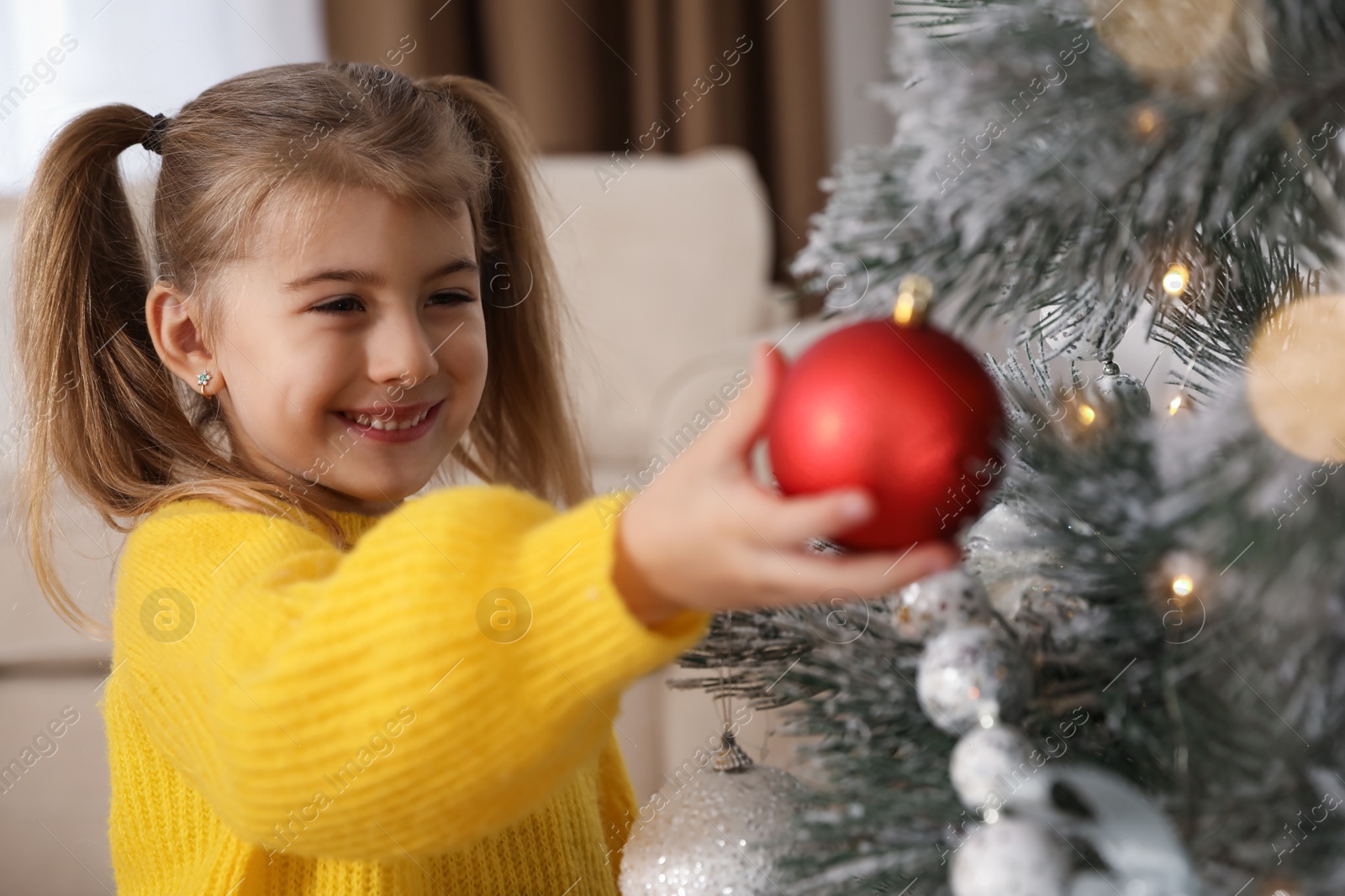 Photo of Cute little girl decorating Christmas tree at home