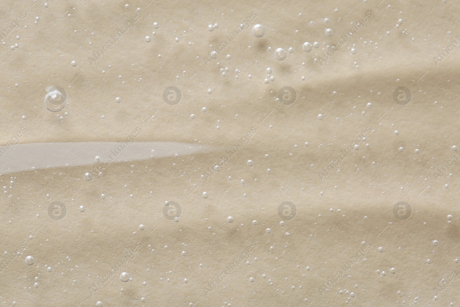 Photo of Clear cosmetic serum on beige background, macro view