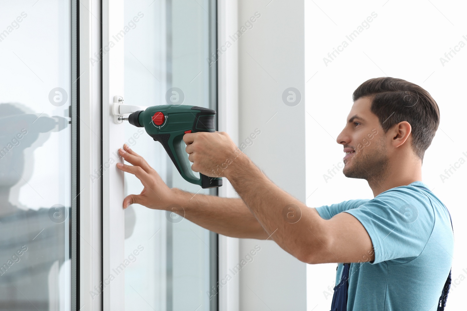 Photo of Construction worker repairing plastic window with electric screwdriver indoors