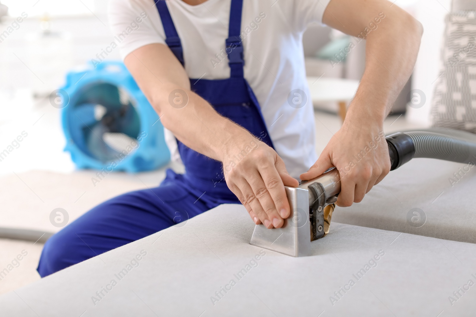 Photo of Dry cleaning worker removing dirt from sofa indoors