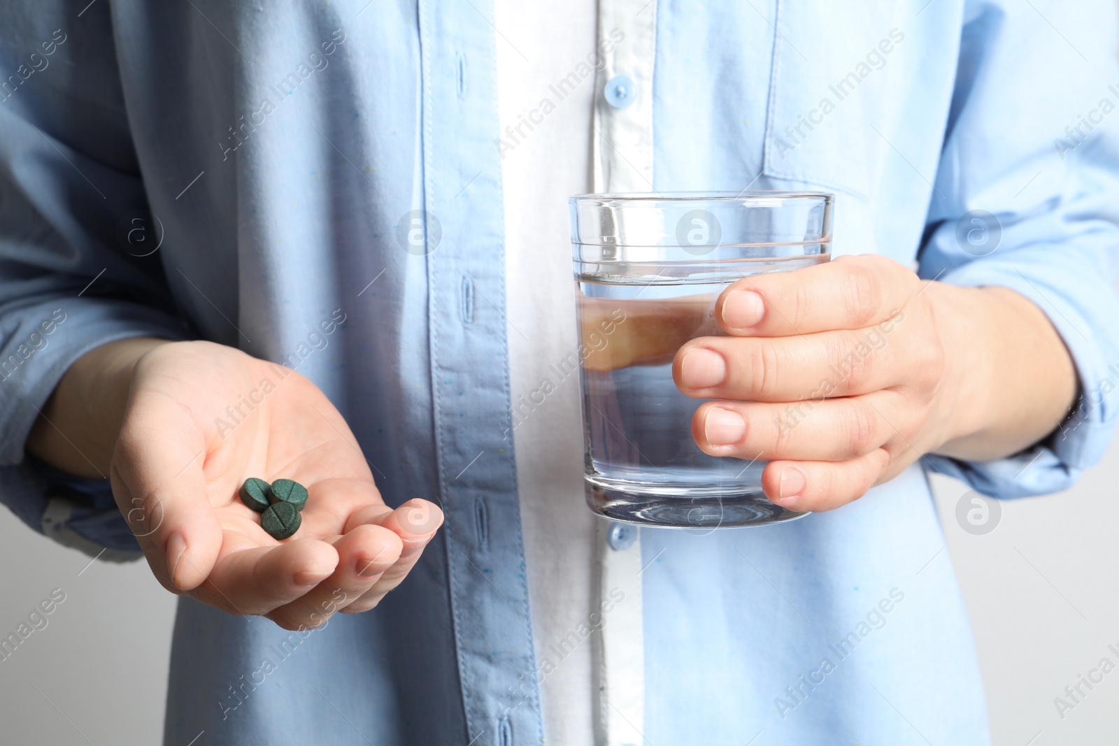 Photo of Woman holding spirulina pills and glass of water, closeup