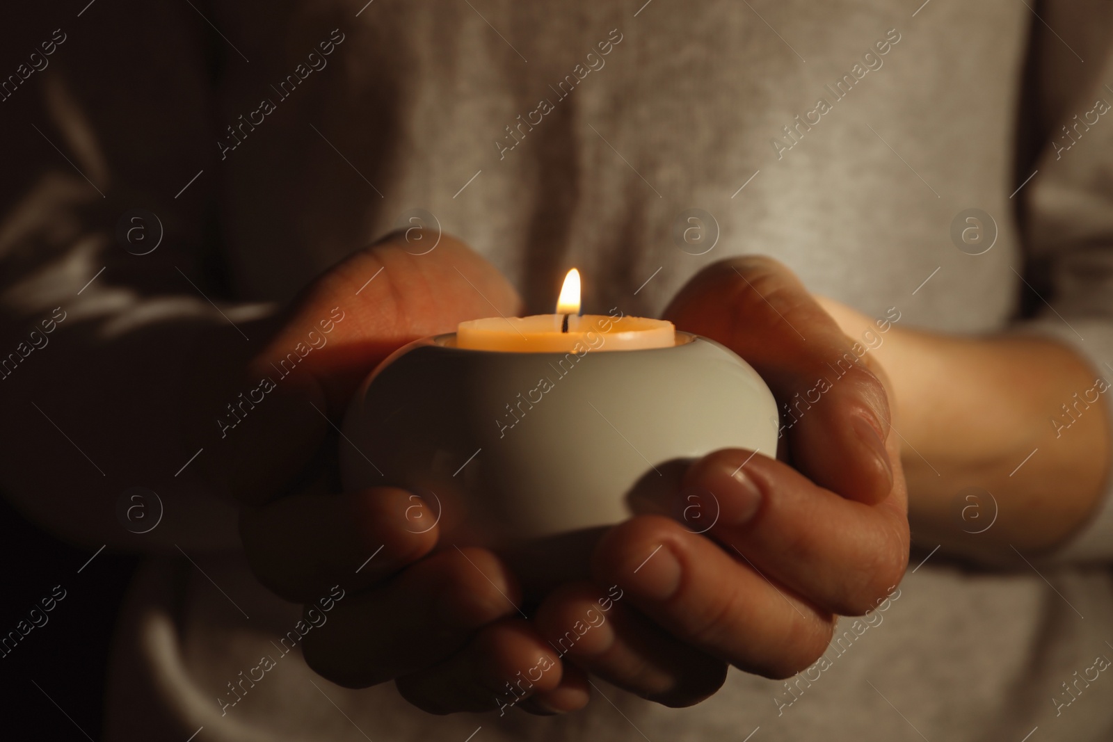 Photo of Young person holding burning candle in darkness, closeup