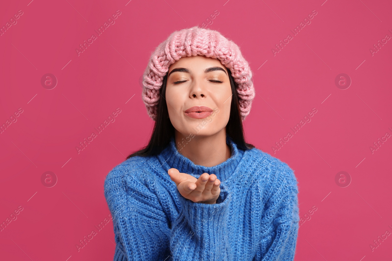 Photo of Young woman wearing warm sweater and hat on crimson background. Winter season