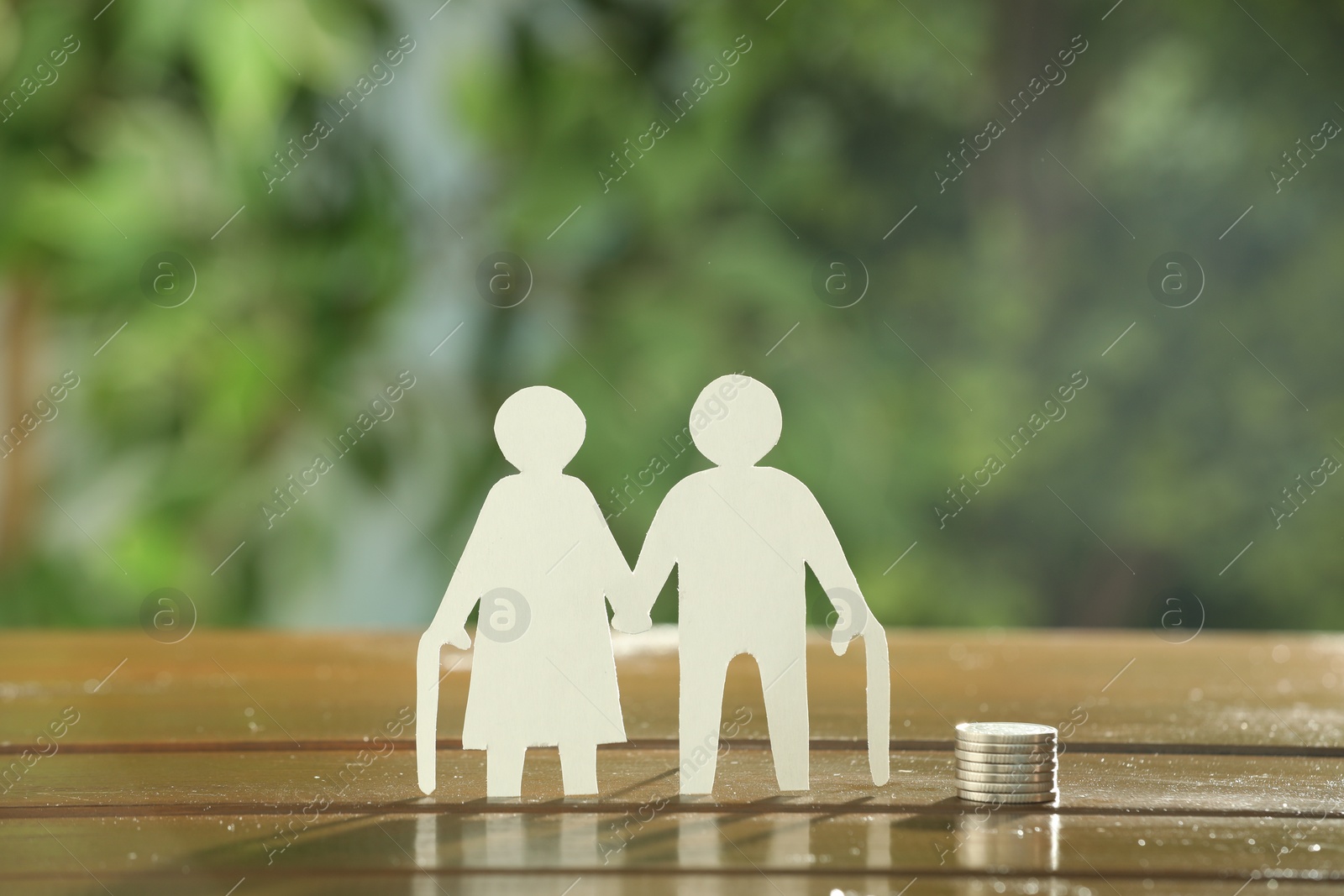 Photo of Pension savings. Figure of senior couple and stacked coins on wooden table outdoors