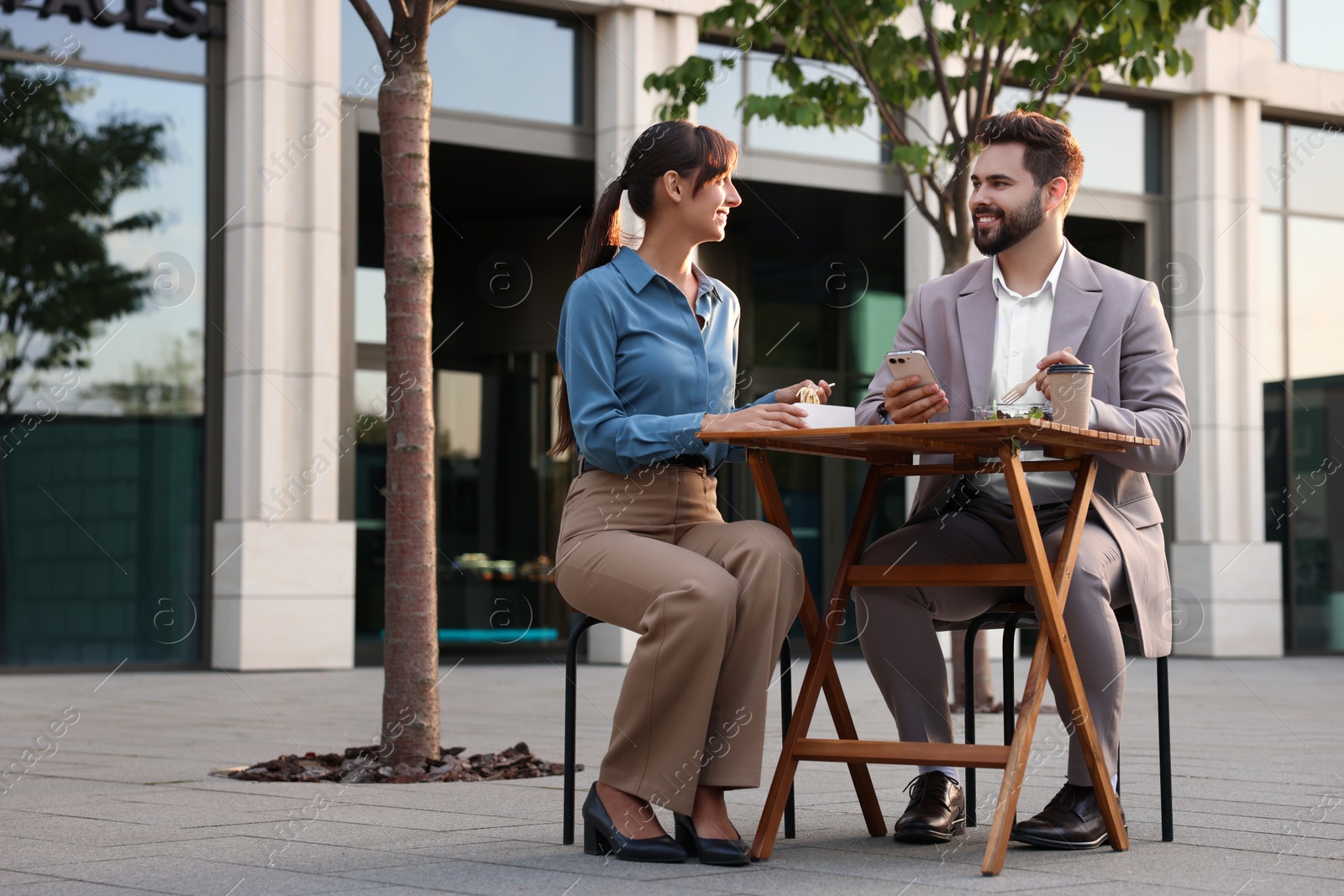 Photo of Happy colleagues having business lunch together at wooden table outdoors,