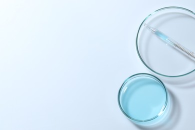 Pipette and petri dishes with liquid on white table, flat lay. Space for text