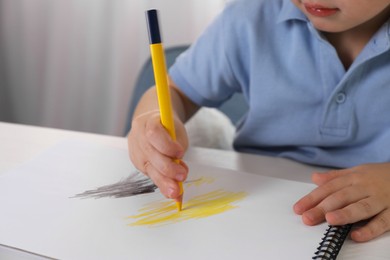 Photo of Little boy drawing with pencil at white table indoors, closeup. Child`s art