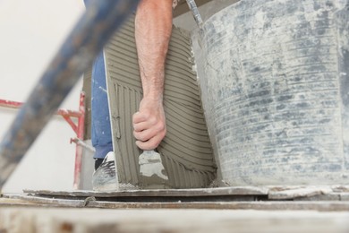 Photo of Worker applying cement on wall tile for installation indoors, closeup