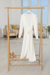 Photo of Beautiful white wedding dress on clothing rack indoors