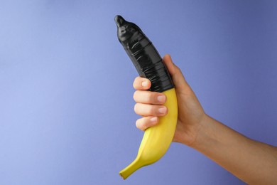 Photo of Woman holding banana in condom on light blue background, closeup and space for text. Safe sex concept