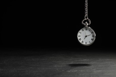 Photo of Beautiful vintage pocket watch with silver chain on black background above dark table, space for text. Hypnosis session