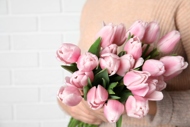 Photo of Woman with beautiful pink spring tulips near white brick wall, closeup
