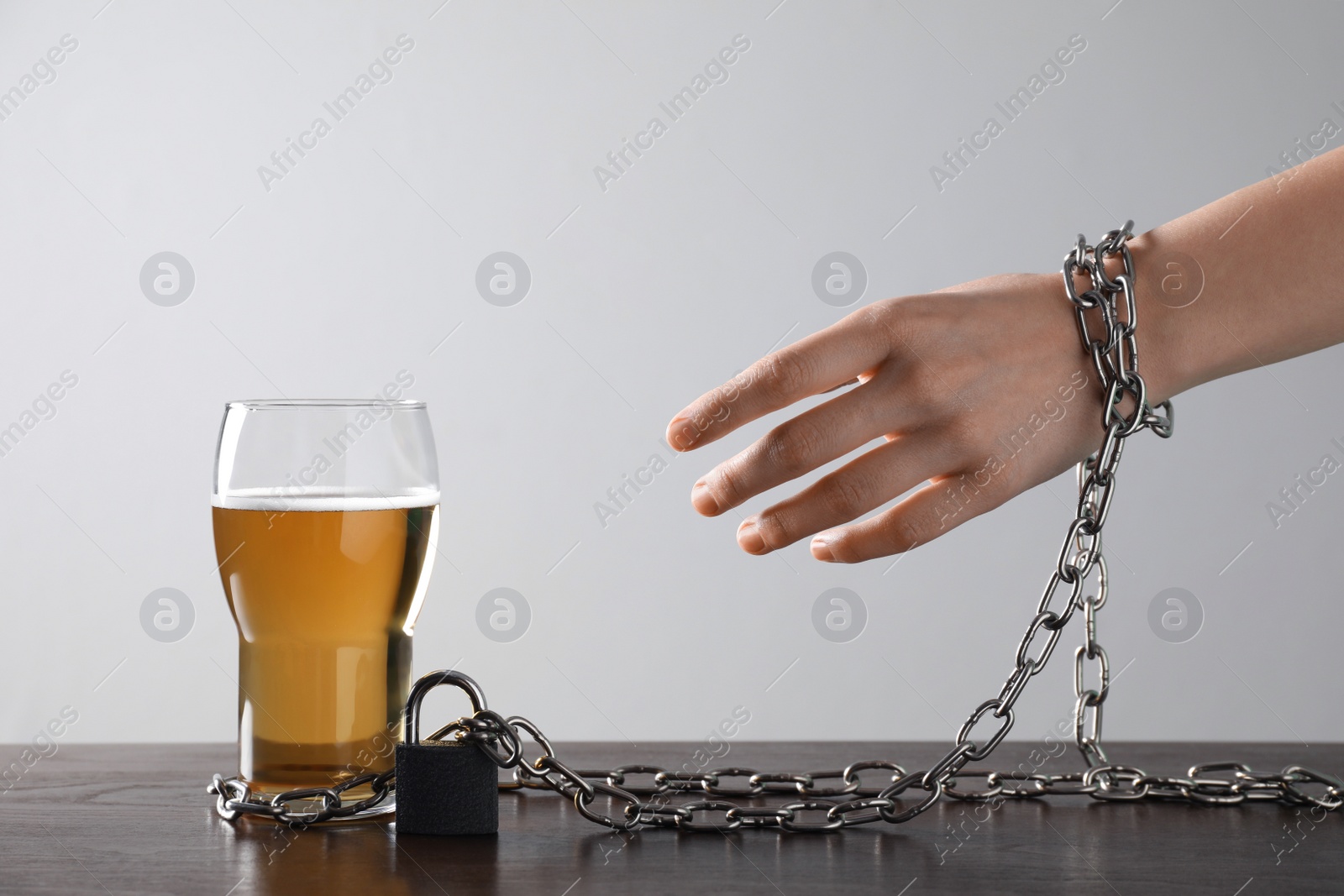 Photo of Woman chained to glass of beer at table against white background, closeup. Alcohol addiction