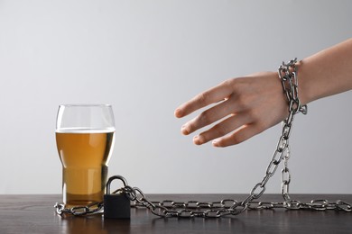 Photo of Woman chained to glass of beer at table against white background, closeup. Alcohol addiction