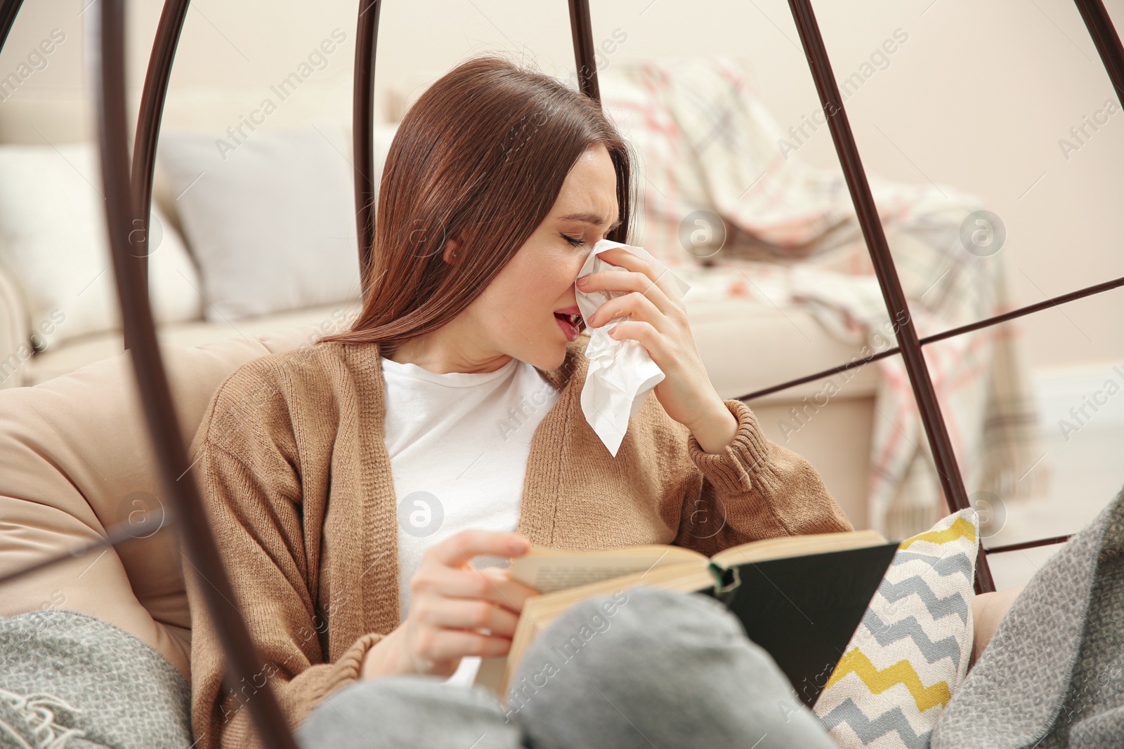 Photo of Sick young woman sneezing while reading book at home. Influenza virus