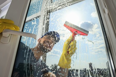 Photo of Man cleaning glass with squeegee indoors, low angle view