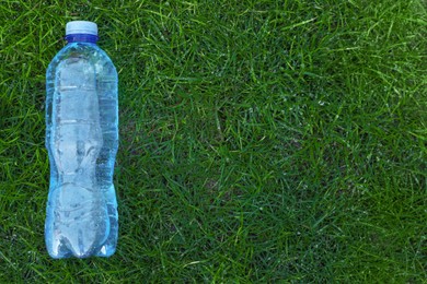 Plastic bottle of water on green grass outdoors, top view. Space for text