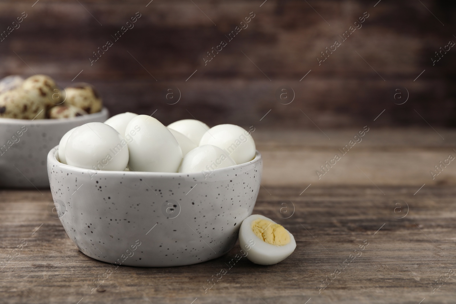 Photo of Many peeled hard boiled quail eggs in bowl on wooden table, closeup. Space for text