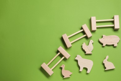 Photo of Wooden animals and fence on green background, flat lay with space for text. Children's toy