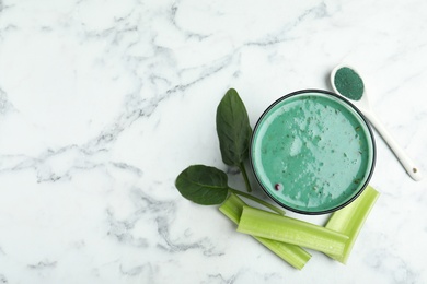 Photo of Glass of spirulina smoothie, powder, spinach and celery on marble background, top view. Space for text
