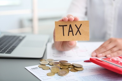 Photo of Woman holding card with word TAX at table