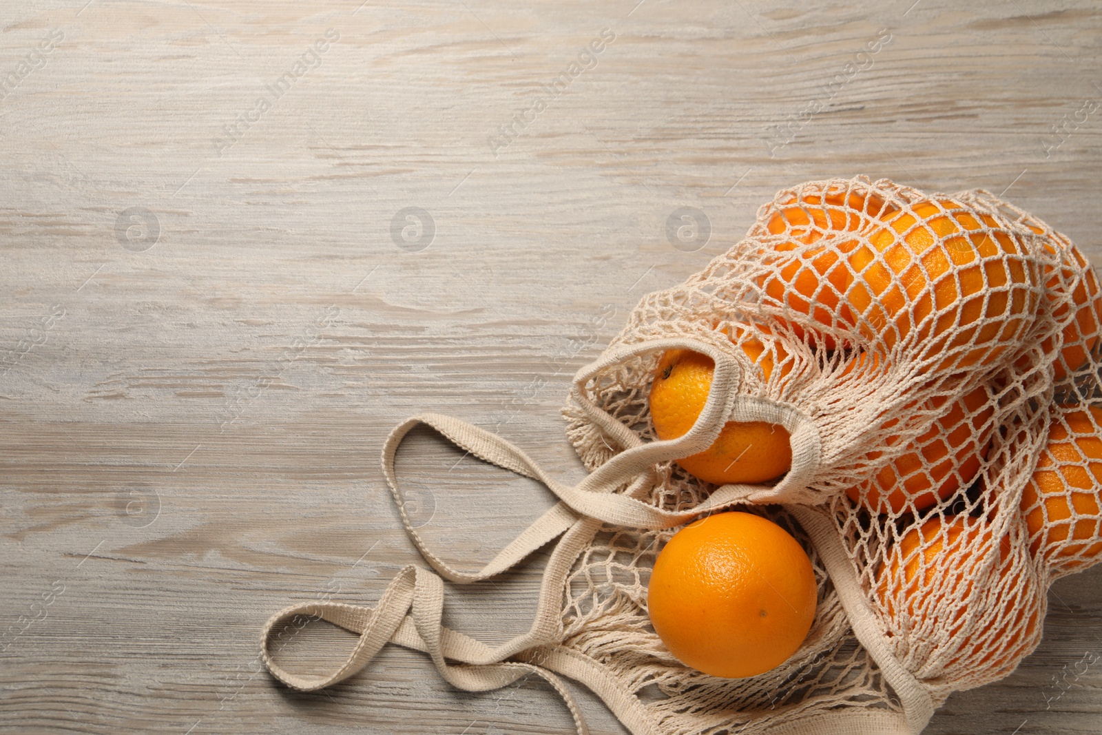 Photo of Many ripe juicy oranges with net bag on wooden table, top view. Space for text