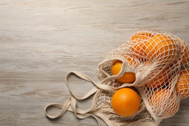 Photo of Many ripe juicy oranges with net bag on wooden table, top view. Space for text