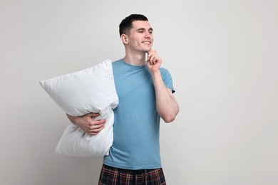 Happy man in pyjama holding pillow on light grey background