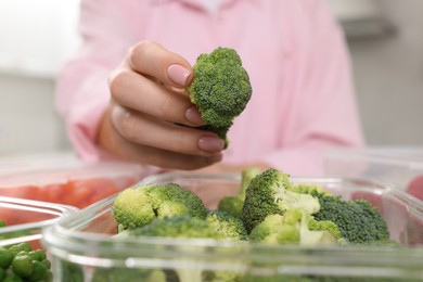 Photo of Woman putting green broccoli into glass container in kitchen, closeup