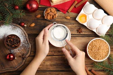 Photo of Woman cooking traditional Christmas cake at wooden table with ingredients, top view