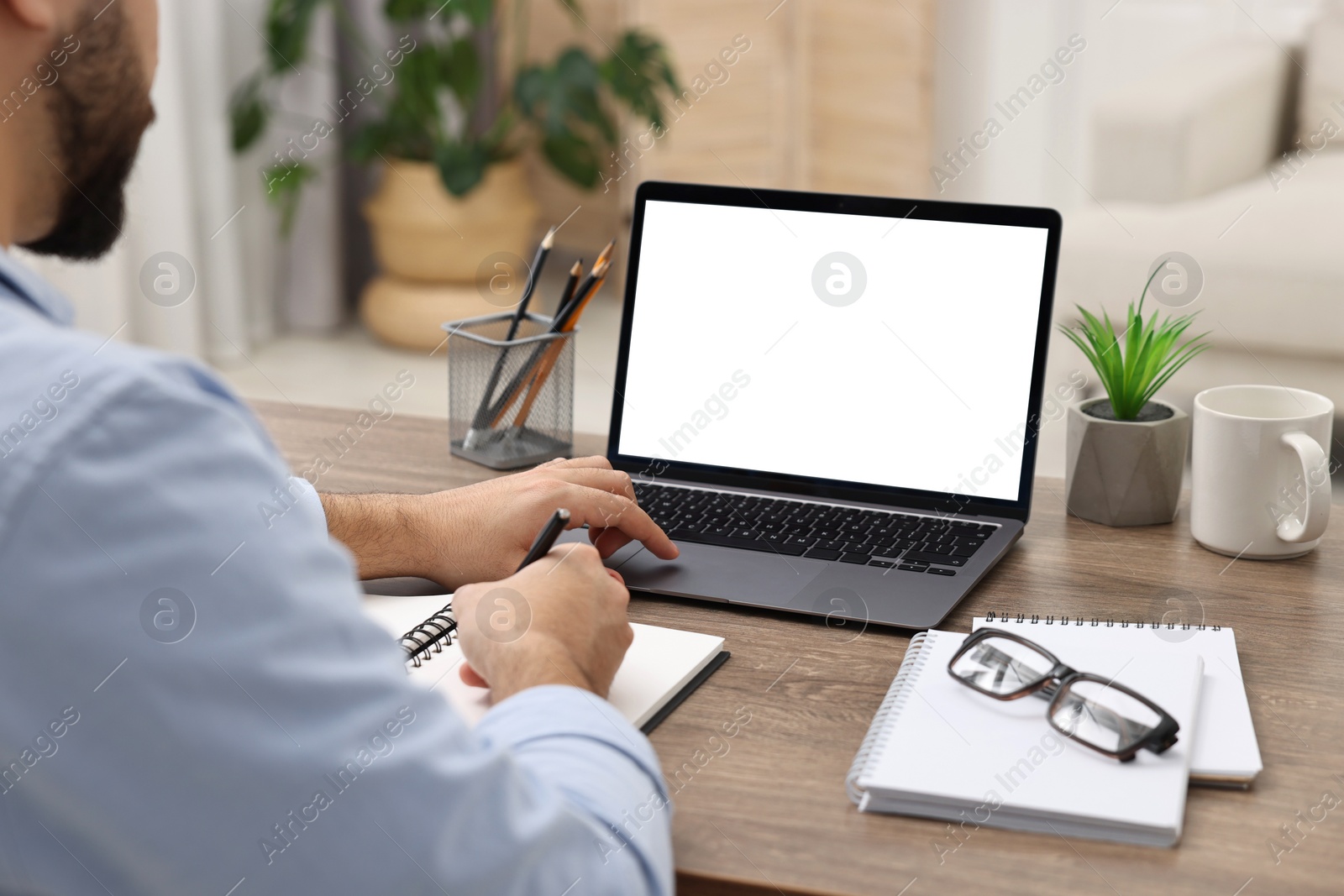 Photo of E-learning. Young man using laptop at wooden table indoors, closeup