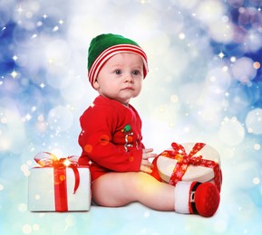 Image of Cute little baby wearing Santa's elf clothes with Christmas gifts on color background