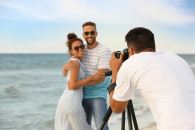 Photographer taking picture of couple with professional camera near sea