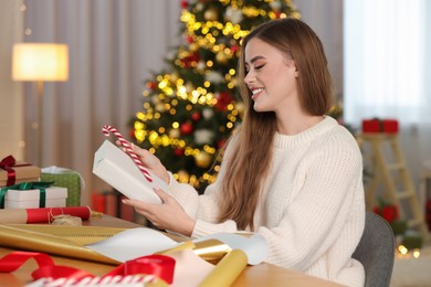 Photo of Beautiful young woman with candy cane decorating Christmas gift at table in room