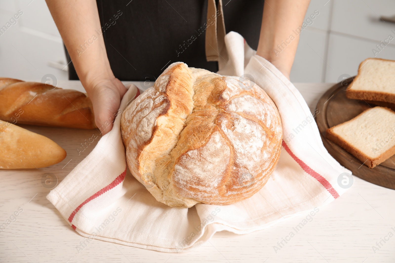 Photo of Baker with loaf of bread at table indoors, closeup