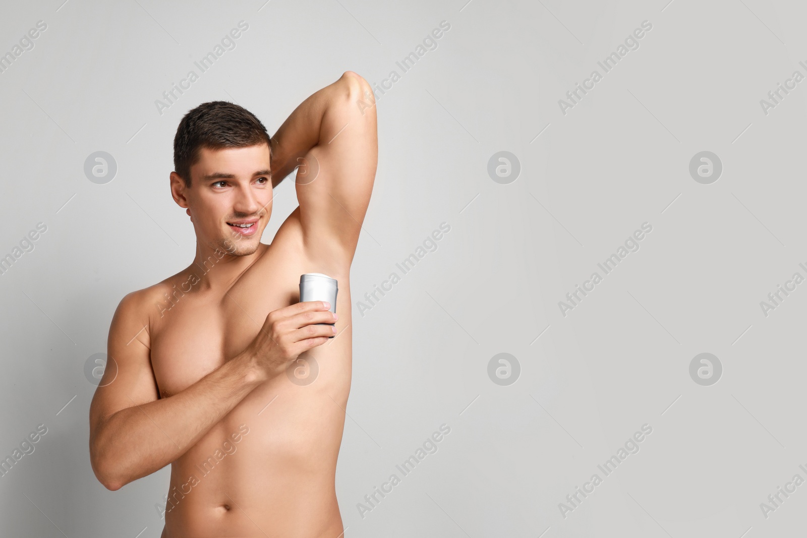 Photo of Young man applying deodorant to armpit on light background. Space for text
