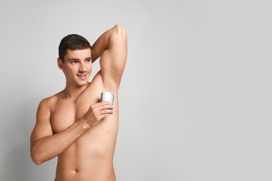 Photo of Young man applying deodorant to armpit on light background. Space for text