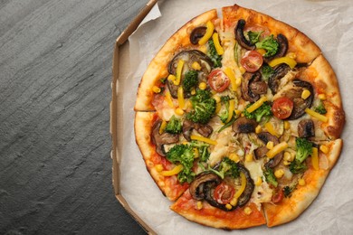 Photo of Delicious vegetarian pizza with mushrooms, cheese and vegetables in box on black table, top view. Space for text