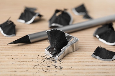 Photo of Pencil, sharpener and shavings on wooden table, closeup