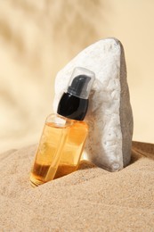 Photo of Bottle of serum and stone on sand against beige background