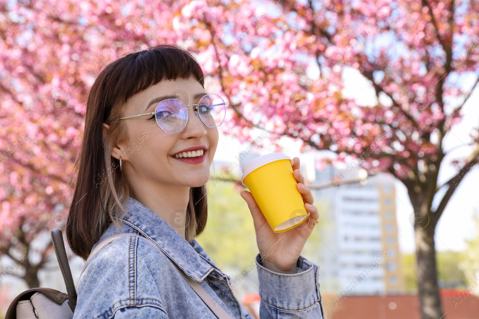 Photo of Beautiful young woman with paper cup near blossoming sakura tree in park