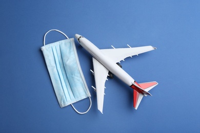 Photo of Toy airplane and protective mask on blue background, flat lay. Travelling during coronavirus pandemic
