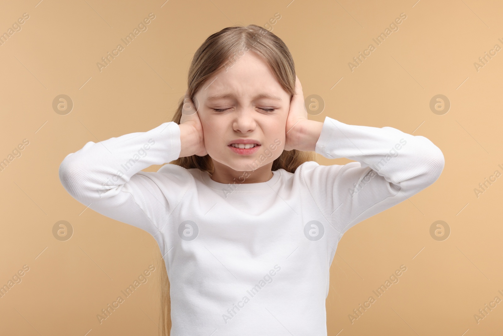 Photo of Hearing problem. Little girl suffering from ear pain on pale brown background